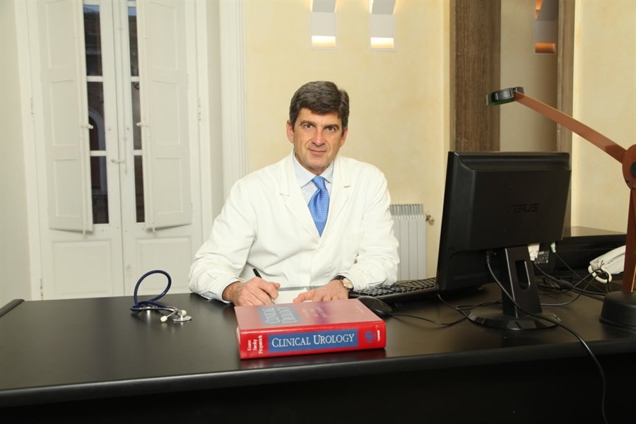 Il dottor Gaetano Ressa in camice bianco alla scrivania dell'ambulatorio, con il fonendoscopio e un manuale di urologia clinica